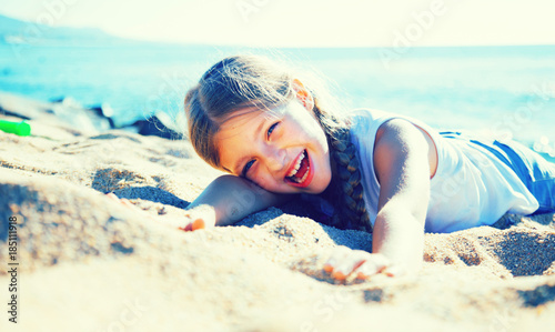 blond child lying on sandy beach of sea coast