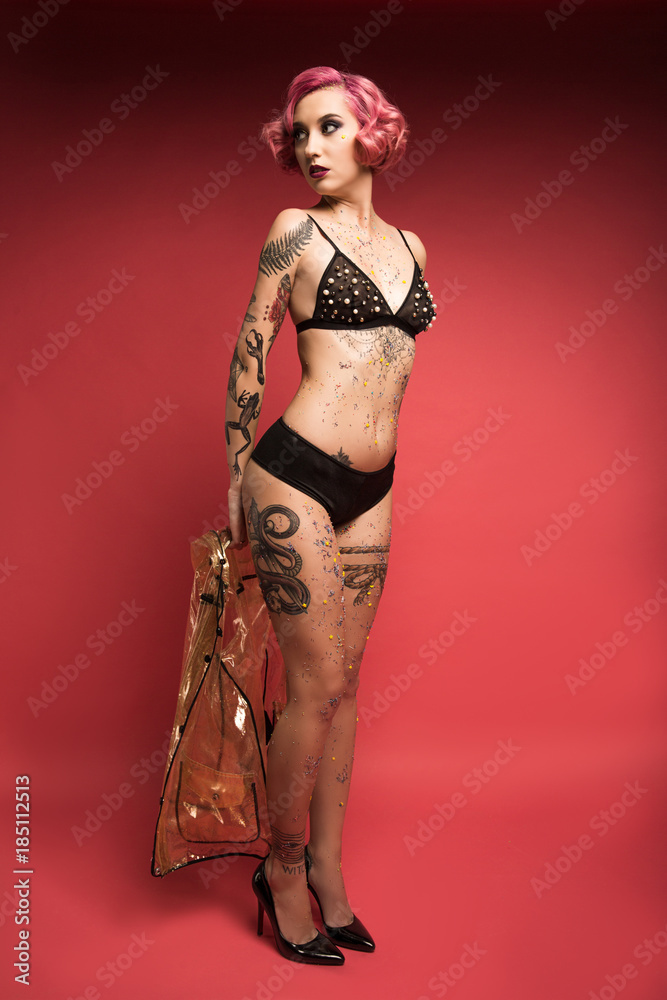 attractive pin up girl with tattoos in lingerie holding raincoat infront of  red background foto de Stock | Adobe Stock