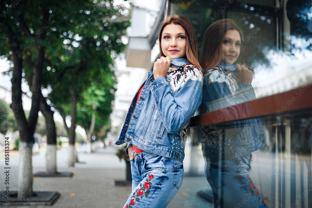 Young woman in blue jeans and red shirt standing in front of mirrored windows. Outdoor.