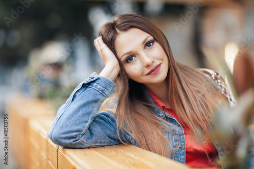 Close up portrait of a beautiful blonde girl Hand Lean Face sitting outdoor in cozy cafe in town. Pretty young model looking at camera and smiling. photo