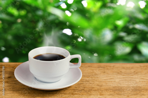 Hot Coffee cup on rustic wooden table on blured fresh green garden background with copy space. Relaxing time with coffee in the morning concept.