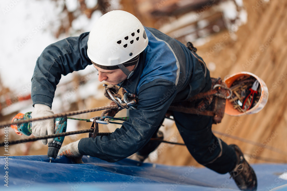 Professional industrial climber in helmet and uniform works at height. Risky extreme job. Industrial climbing at construction site