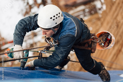 Professional industrial climber in helmet and uniform works at height. Risky extreme job. Industrial climbing at construction site