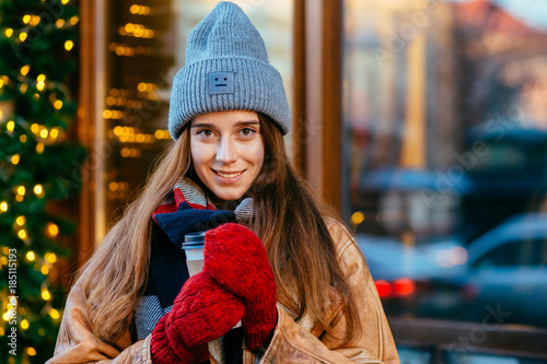 Playful hipster woman dressed in winter clothes walking on street, injoying the winater holiday over shop window with garland. Close up. City lifestyle concept. photo