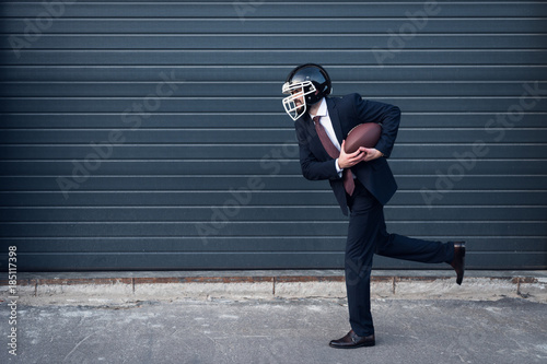 side view of young businessman in suit and rugby helmet with ball in hands running on street photo