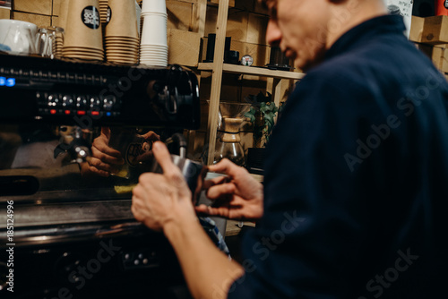 Handsome barista preparing cup of coffee for customer in coffee shop. Retro picture with little noise.