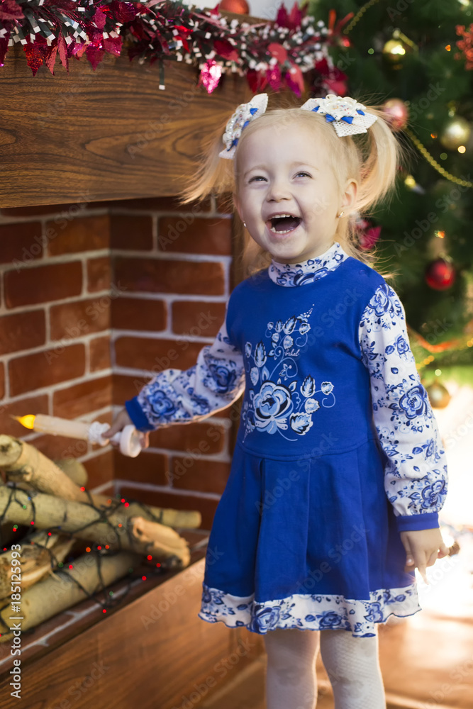 Beautiful little girl meets Christmas. A funny beautiful girl in a blue dress is having fun near the Christmas tree at home. Beautiful little girl meets Christmas. A funny beautiful girl in a blue dress is having fun near the Christmas tree at home.