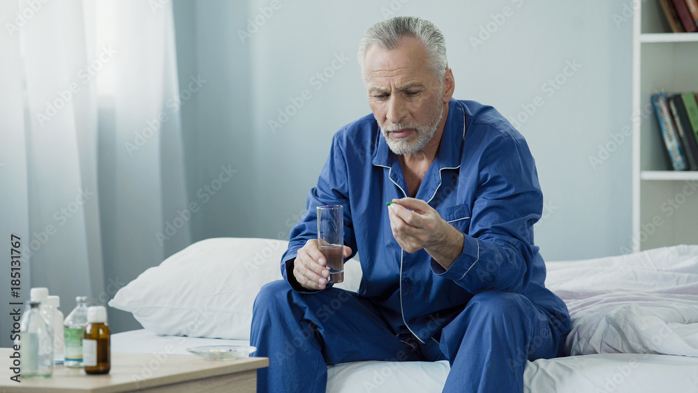 Fototapeta premium Male pensioner taking daily vitamin complex to maintain genitourinary system