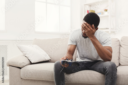 Unhappy young man at home playing video games and loses © Prostock-studio