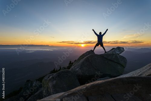 Silhouette man with arms raised standing on rocks against sky at Mount Pilchuck State Park during sunset photo