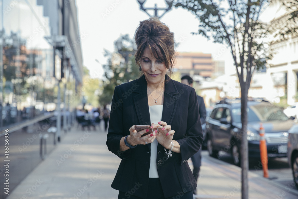 Businesswoman using smartphone while walking on the footpath Businesswoman using smartphone while walking on the footpath