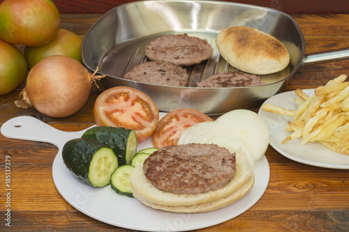 Una hamburguesa sobre el pan y los ingredientes vegetales, una sartén
 con hamburguesas cocinadas