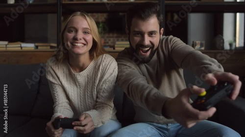 Cheerful day. Delighted couple sitting on the sofa while using joypads and playing video games