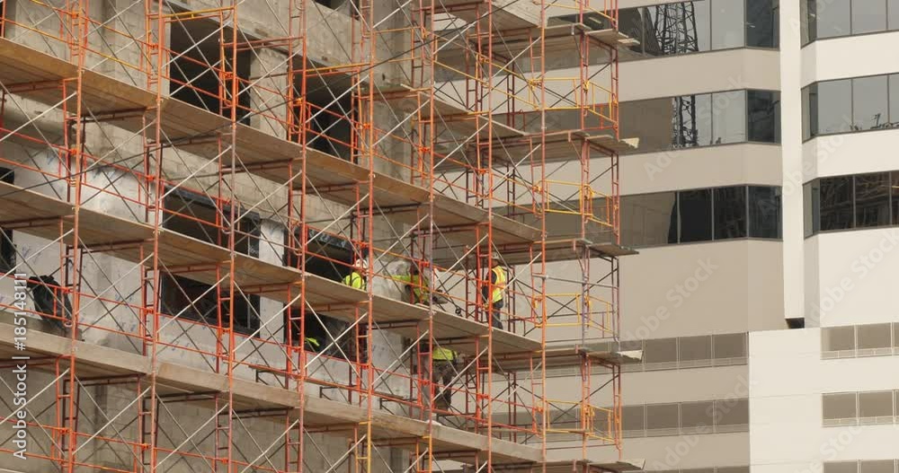 A long shot of construction workers on scaffolding on the side of a building in a large city.  	