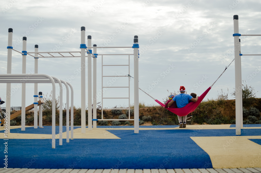 Naklejka premium Family having fun lying on hammock in outdoors garden background. Back view of happy people together enjoying healthy relaxing lifestyle. Cool emotion parenting, recreation leisure enjoyment