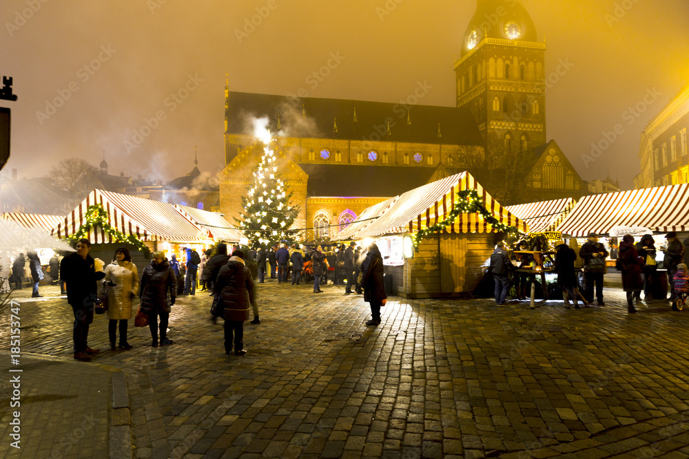 Traditional Christmas street market in Latvia on cold winter day, magnificent church in background. People are eating, drinking, having fun.