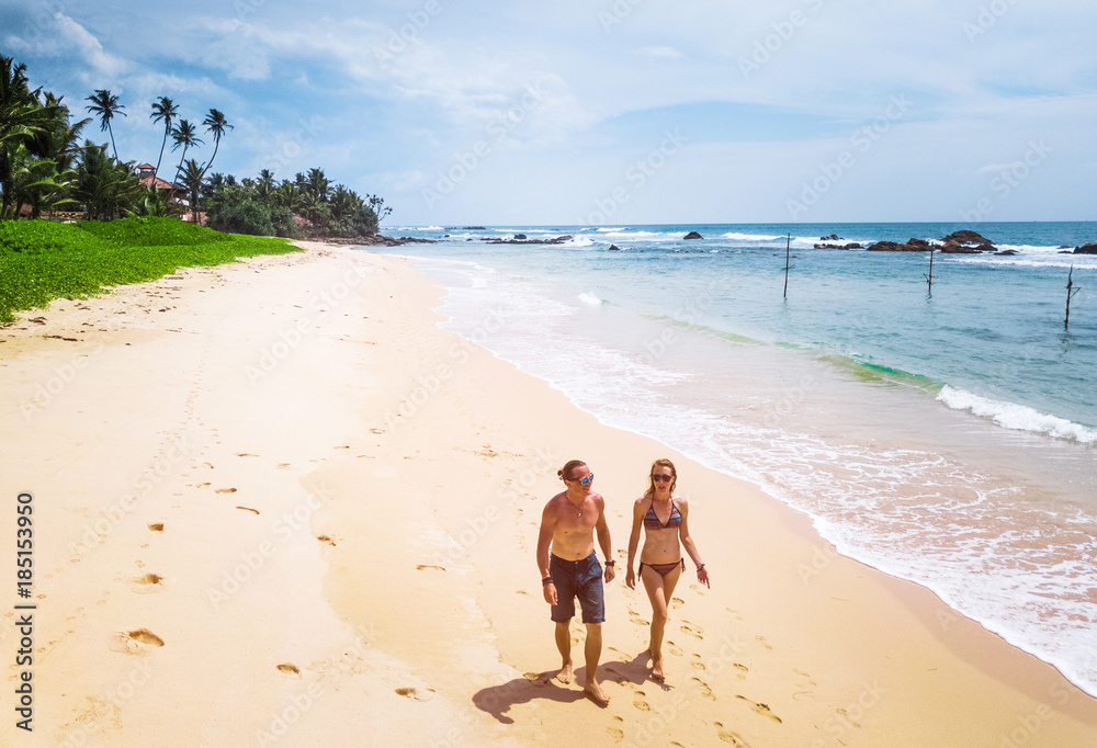 Couple walks along the tropical sandy beach at sunny day. Honeymoon and family vacation concept