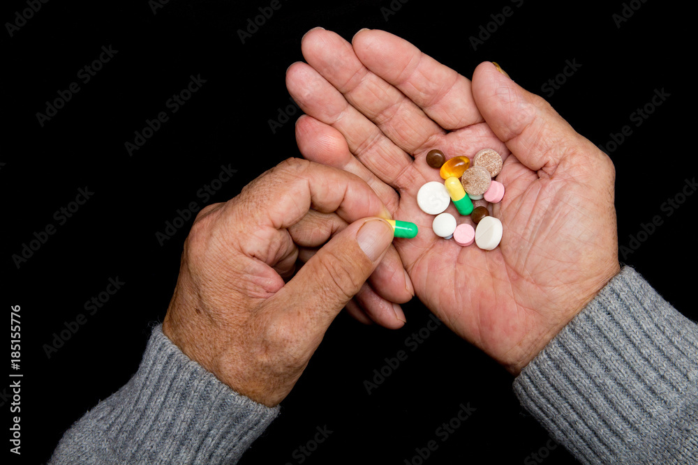 An elderly man holds a lot of colored pills in old hands on a dark background. Painful old age. Health care of older people. Top View An elderly man holds a lot of colored pills in old hands on a dark background. Painful old age. Health care of older people. Top View