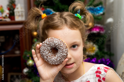 Happy little cute girl with a donut on Christmas background. The child having fun with a doughnut. Sweets for children. photo