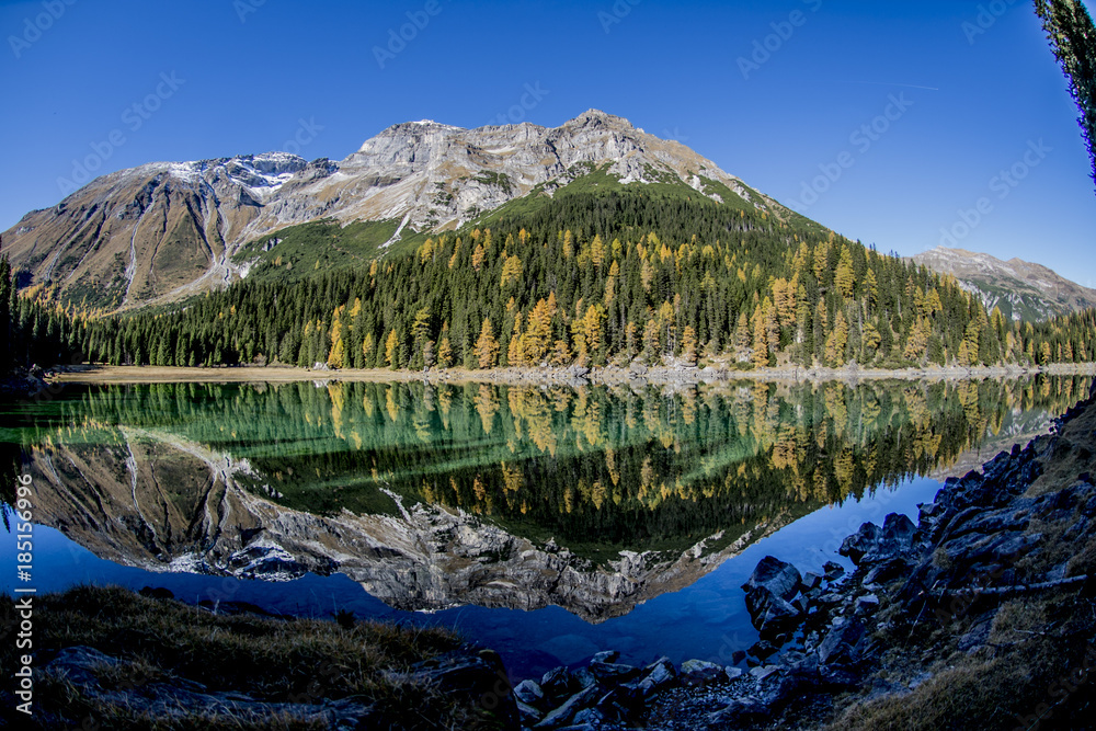 Obernbergersee in autumn with a surface reflection and a blue sky