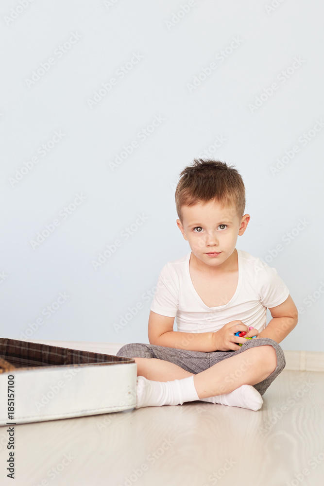 the boy sits on the white suitcase in the room