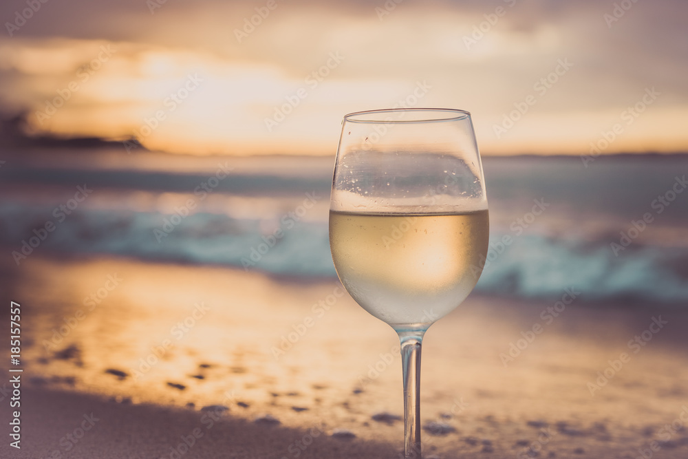 A glass  of white wine on the beach at sunset. Travel vacations concept.