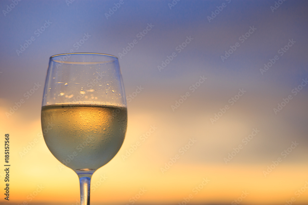 Wineglass of white wine at sunset dramatic sky background. Closeup. Travel vacations concept.