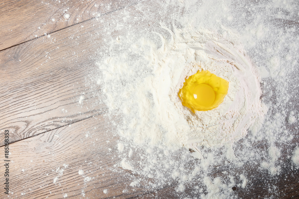 The top view of an egg, beaten into flour, cooking dough against the background of a wooden table. Flat lay The top view of an egg, beaten into flour, cooking dough against the background of a wooden table. Flat lay