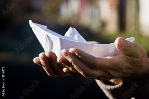 Paper boat in old wrinkled hands of grandmother close-up