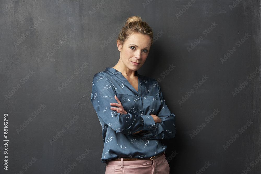 Studio shot of a confident mature woman looking at camera while standing against at gray background.