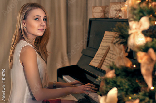 Girl playing piano near Christmas tree