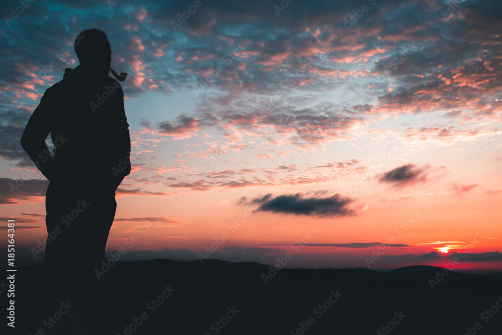 Silhouette of a man with a Smoking pipe on a background of red sky and sunset Silhouette of a man with a Smoking pipe on a background of red sky and sunset