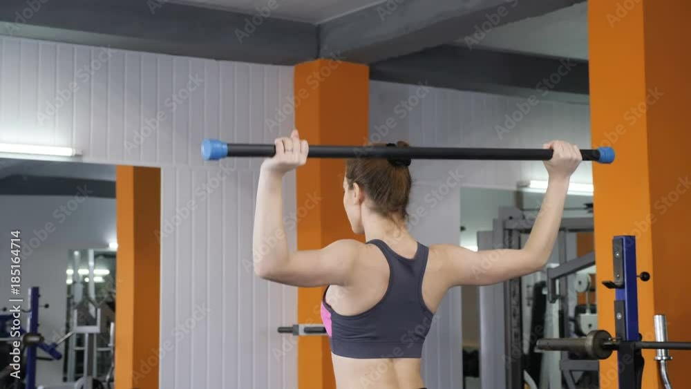Young beautiful sporty girl lifting barbell bar in gym, shoulder exercise, back side view. 60 fps Young beautiful sporty girl lifting barbell bar in gym, shoulder exercise, back side view. 60 fps