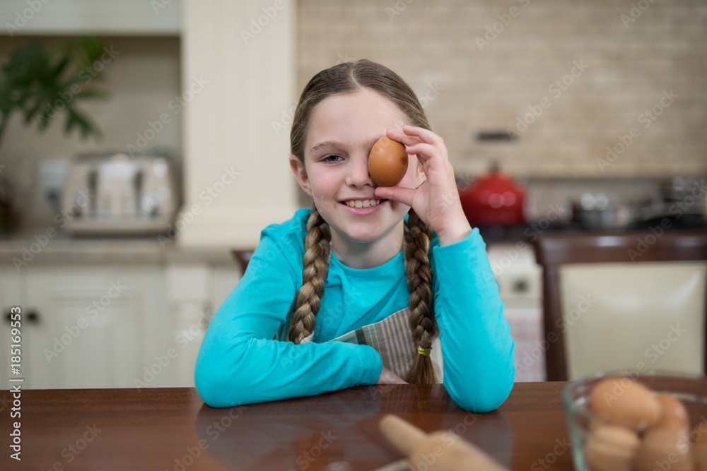 Girl holding egg while sitting on table in the kitchen Girl holding egg while sitting on table in the kitchen
