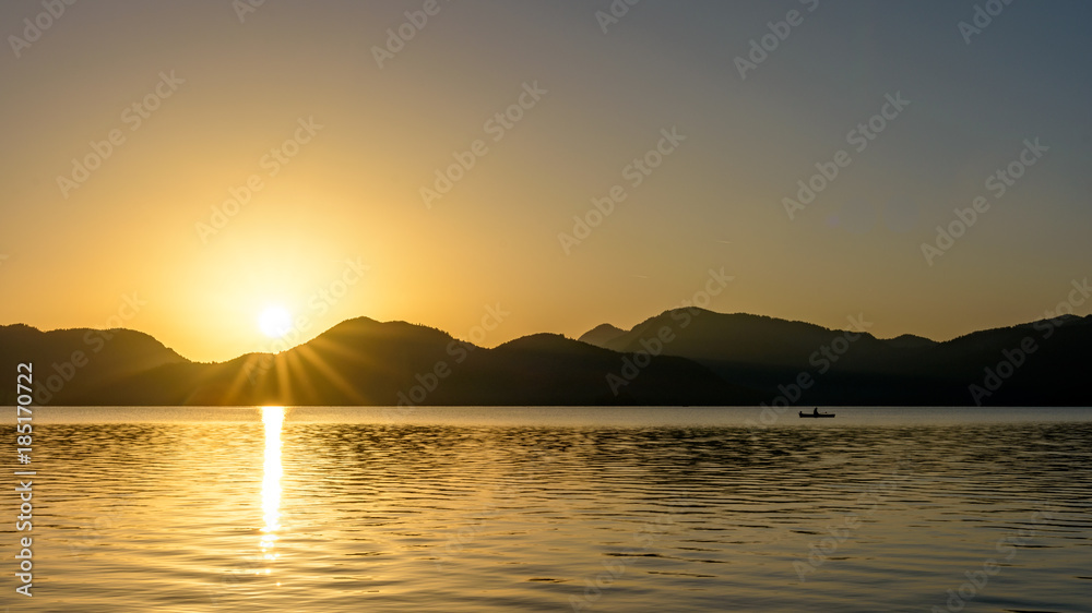 Sunrise over mountains and lake with canoeist.