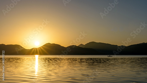 Sunrise over mountains and lake with canoeist.