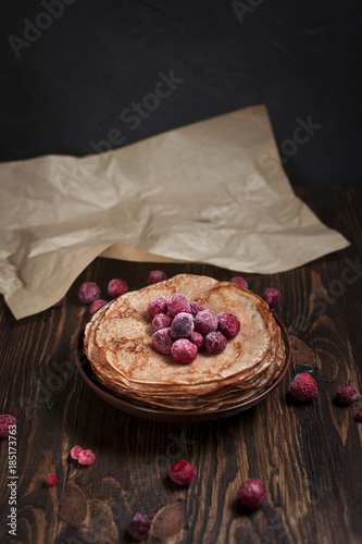 pancakes with frozen berries pile in a brown plate on a dark wooden table on a dark gray background