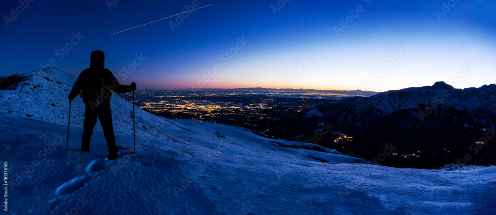 Obraz premium Hiker looking at a winter mountain landscape while the ISS (International Space Station) leaves his trail in the evening sky.
