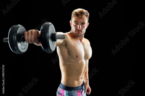 Build muscle and gain strength. Strong guy with sculpted torso lifting dumbbells on black.