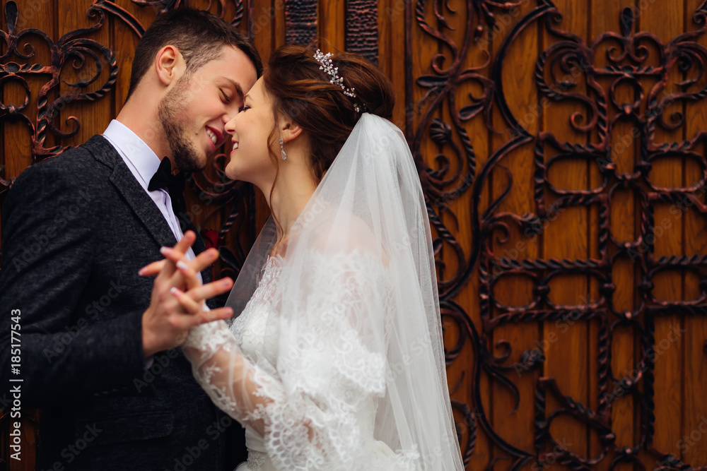 happy smiles of newlyweds who hold hands on the background of refined wooden doors