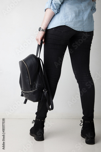 Women's legs in the city street. Blue cropped denim jeans, black high heel sandals and black backpack. Trendy stylish casual outfit.