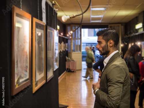Side view of trendy confident man exploring art pieces in gallery. 