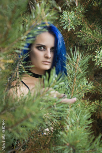Beautiful woman with dark blue hair dressed in black dress in the magic forest
