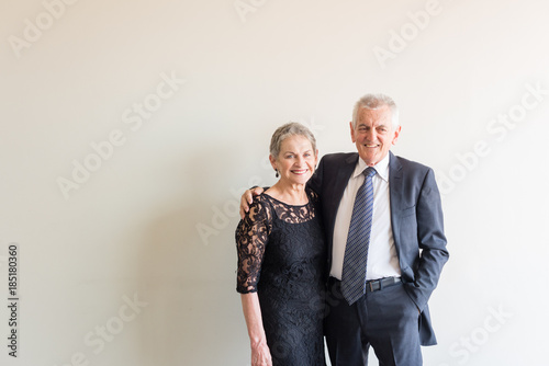 Midlength view of older couple dressed in elegant clothing, including man with arm around woman - senior romance concept (selective focus)