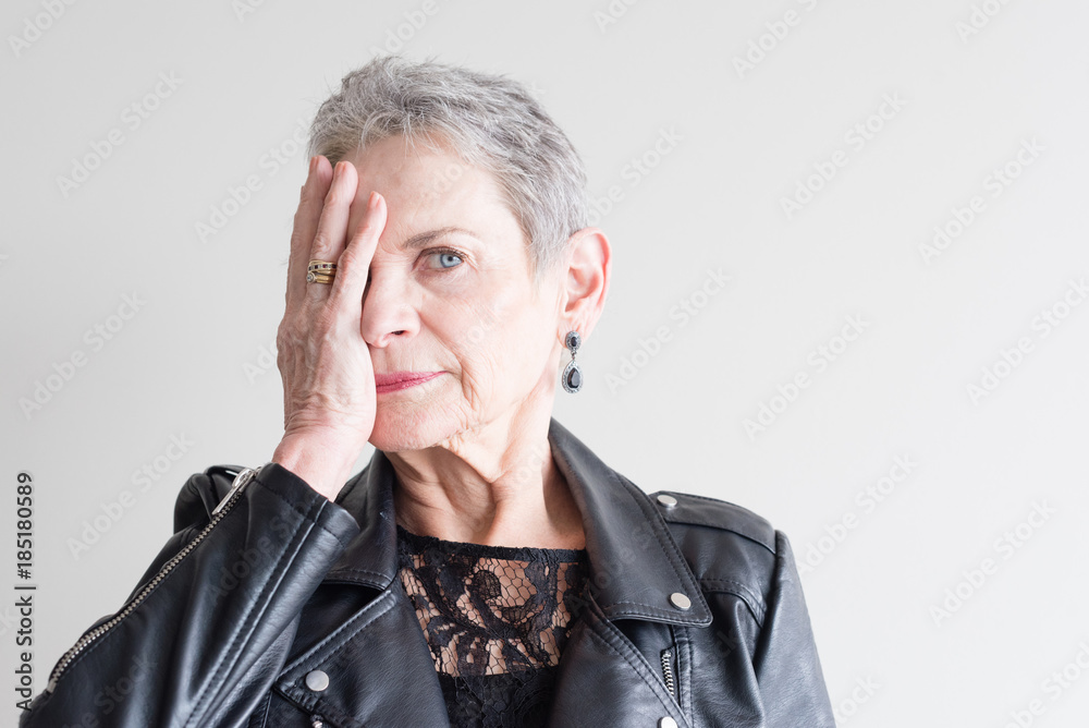 Head and shoulders view of beautiful older woman with short grey hair in black jacket covering half of her face with her hand (selective focus) Head and shoulders view of beautiful older woman with short grey hair in black jacket covering half of her face with her hand (selective focus)