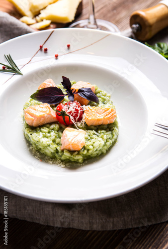Risotto with basil and salmon in a white plate on a dark wooden background top view