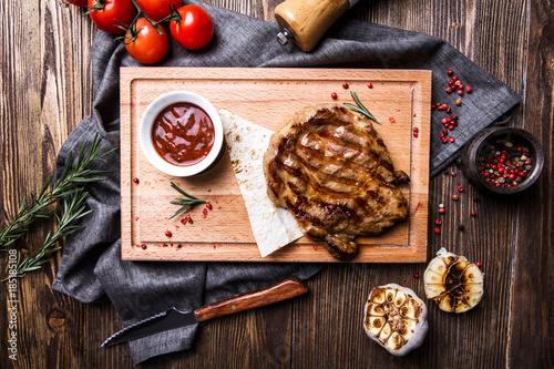 Fototapeta Naklejka Na Ścianę i Meble -  Juicy grilled steak with tomato sauce on a board on a dark wooden background top view