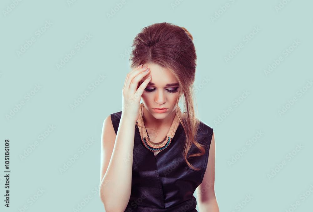 Sad and beautiful. Portrait of a stressed out young woman with worried face expression hand on her head looking down isolated light green background Sad and beautiful. Portrait of a stressed out young woman with worried face expression hand on her head looking down isolated light green background