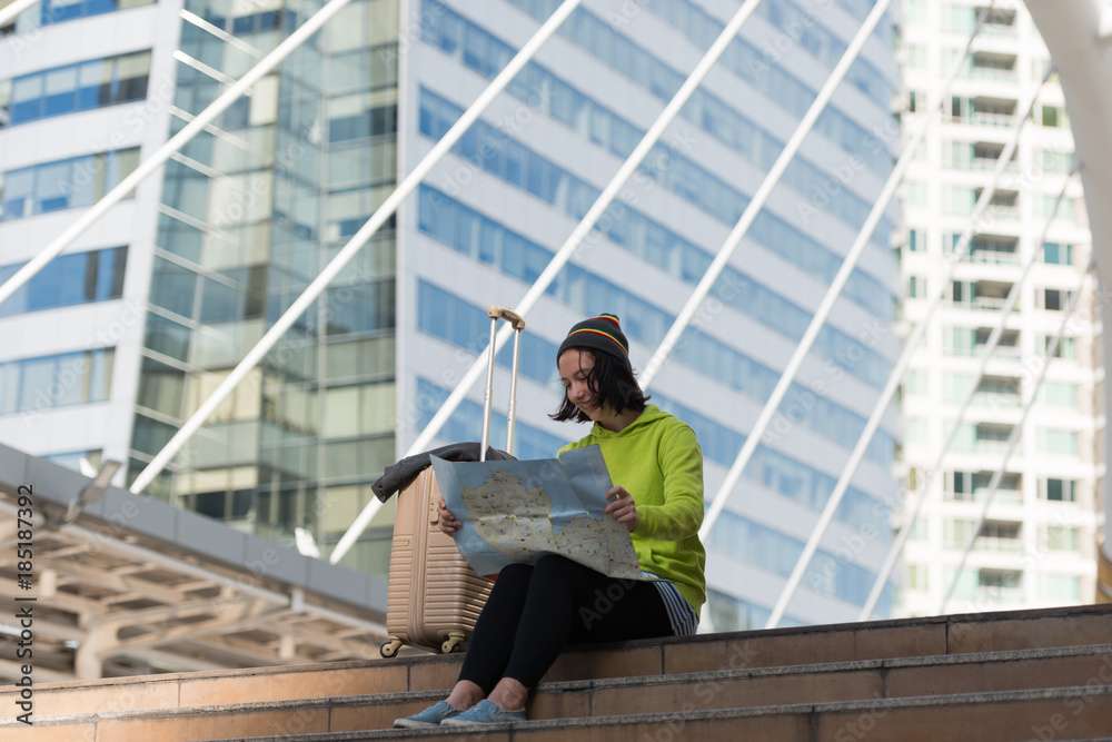 Happy female tourist with suitcase exploring map while sitting in city building, Travel concept Happy female tourist with suitcase exploring map while sitting in city building, Travel concept