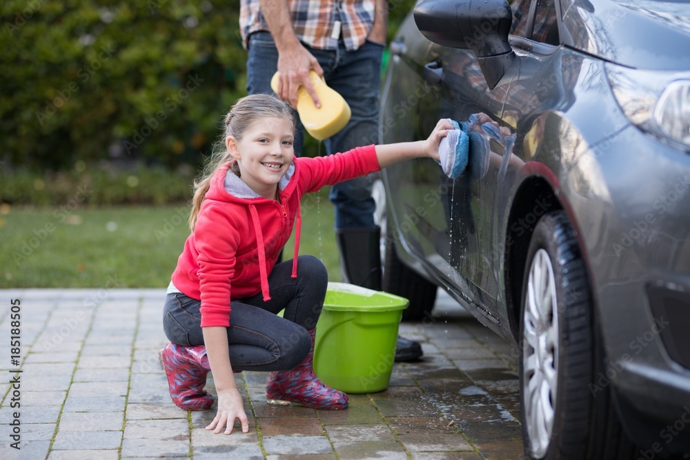 Naklejka premium Teenage girl washing a car on a sunny day